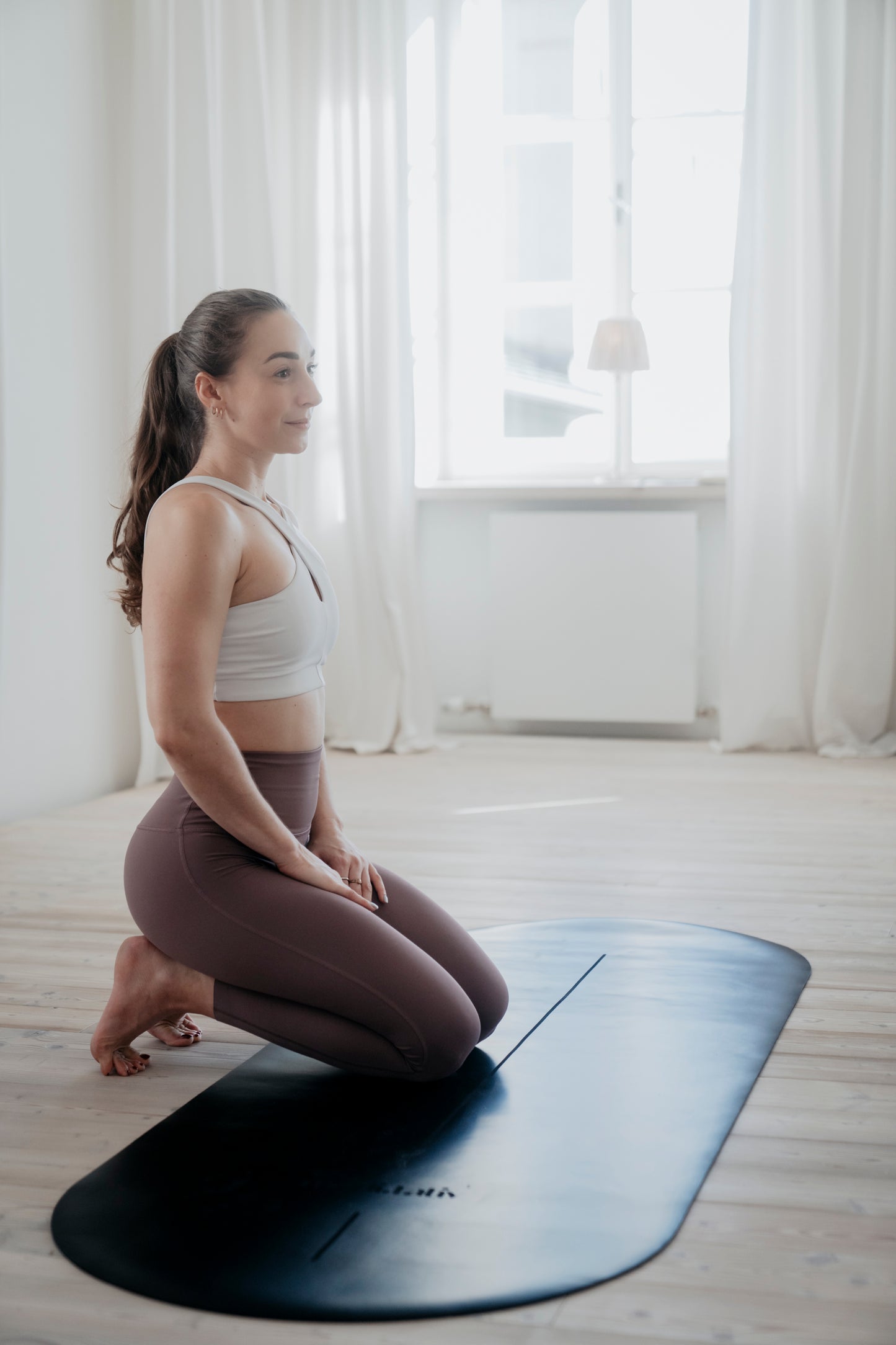 Frau in kniender Position auf der ALL BLACK Yogamatte, hergestellt aus Naturkautschuk mit PU Oberfläche für perfekte Stabilität und Komfort.